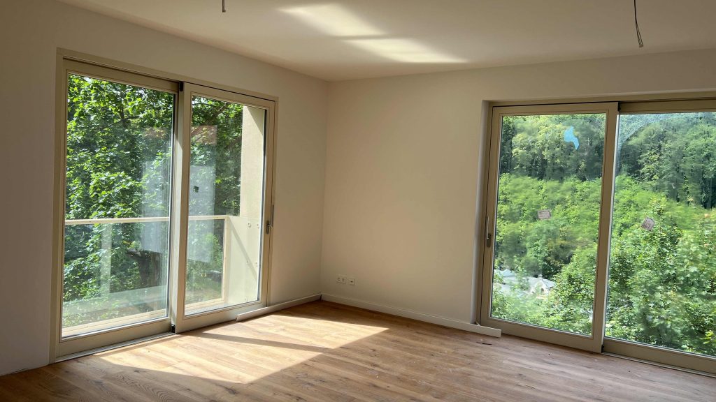 2025-06-11-15.41.53 Helles Wohnzimmer mit Holzparkett, großen Glasschiebetüren und Blick auf grüne Waldlandschaft