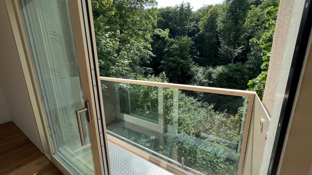 2025-06-11-15.42.14 Balkon mit Glasschiebetür und Waldblick über dichte grüne Baumkronen