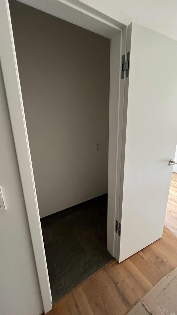 2025-06-11-15.43.40 Offene Türe zu dunklem Kellerraum mit heller Wand und Holzparkett davor
