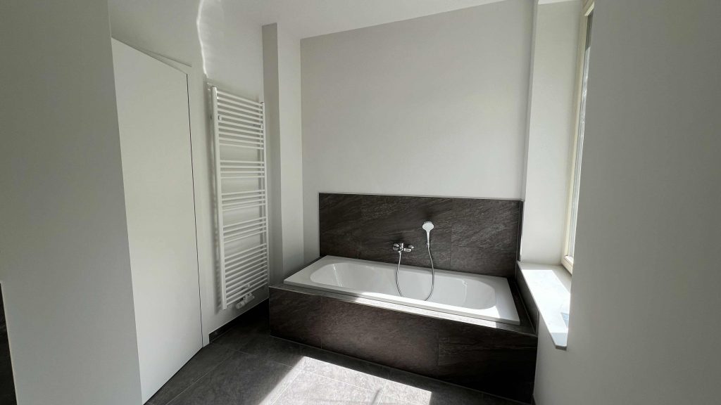 2025-06-11-15.44.04 Modernes Badezimmer mit schwarzer Badewanne, weißem Waschbeckenbereich, Handtuchheizkörper und Fenster