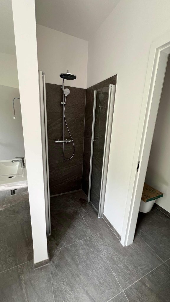 2025-06-11-15.44.18 Modernes Badezimmer mit begehbarer Duschkabine, schwarzen Wandfliesen, Regenduschkopf und Handbrause