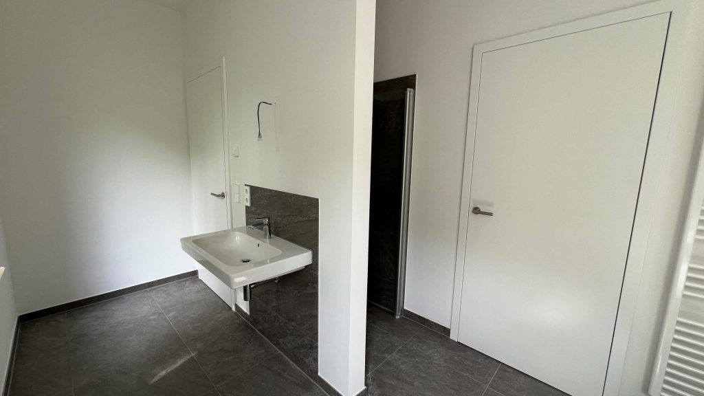 2025-06-11-15.44.47 Modernes Badezimmer mit weißem Waschbecken, grauem Fliesenbelag, Spiegel und weißen Türen