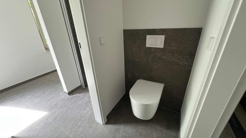 2025-06-11-15.45.06 Modernes Badezimmer mit weißem Toilettenbecken, dunklen Wandfliesen und grauem Fliesenboden