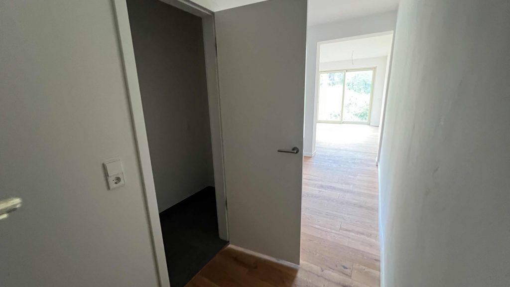2025-07-10-12.05.03 Flur mit offener Tür zu dunklem Raum, Durchgang zu hellem Wohnbereich mit Holzboden und Fenster