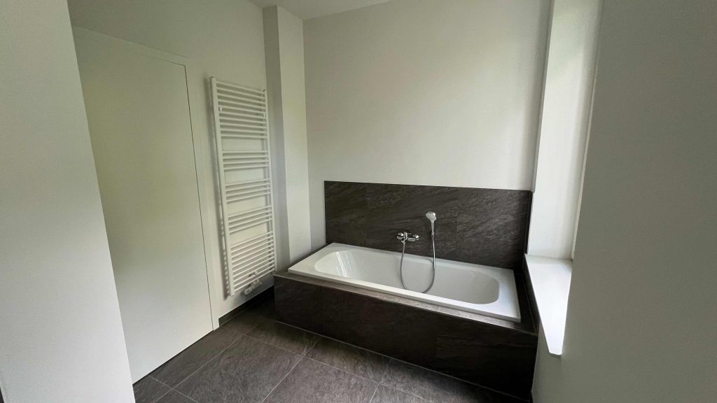2025-07-10-12.05.59 Modernes Badezimmer mit freistehender Badewanne, dunkler Wandverkleidung, weißem Handtuchheizer und Fenster