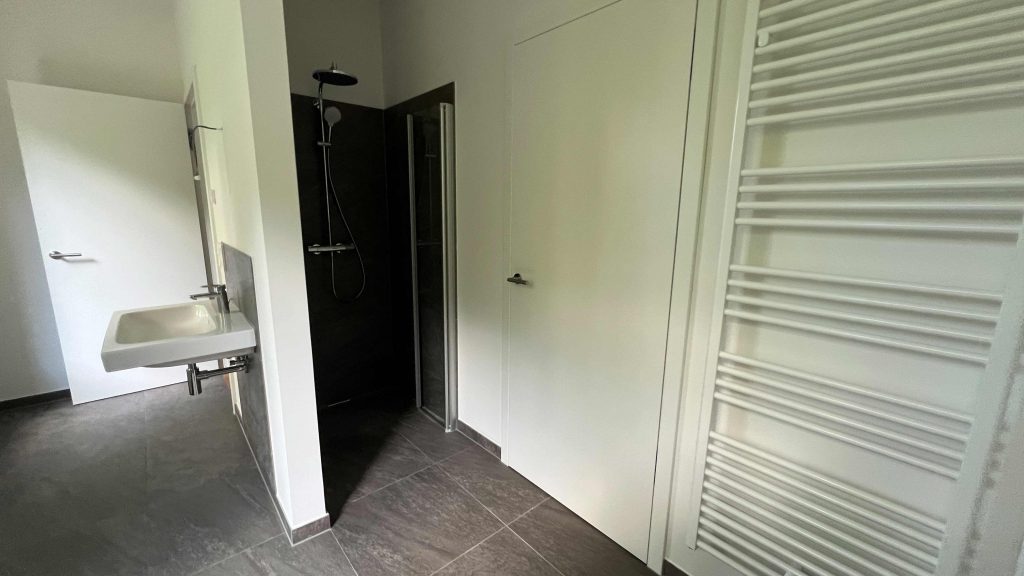 2025-07-10-12.06.24 Modernes Badezimmer mit schwarzer Duschkabine, weißem Waschtisch links, Handtuchheizkörper rechts und dunklem Fliesenboden