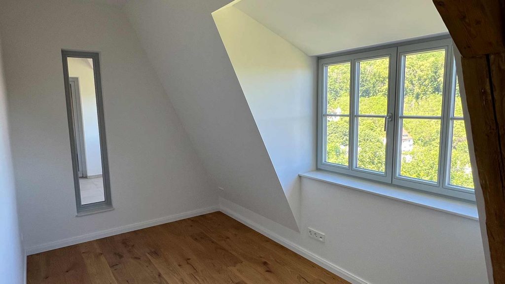 Dachzimmer Holzboden große Fenster Obergeschoss Helles Dachzimmer mit Parkett, großem Fenster zur Gartenansicht, Spiegeltür links und Steckdose an der Wand