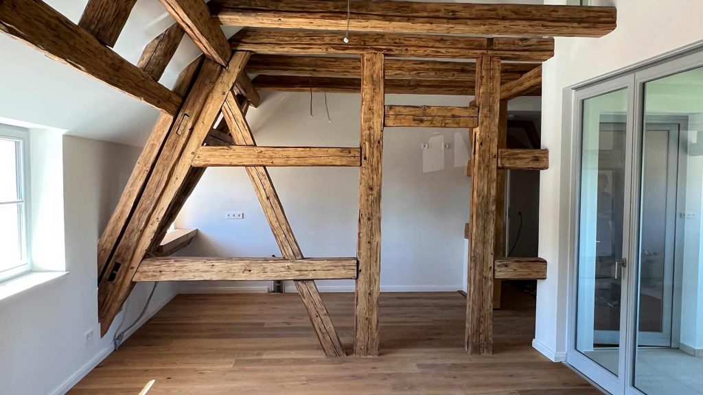 Holzbalken Dachausbau Wohnraum mit Glaschiebetüren Leerer Dachraum mit massiven Holzkonstruktionen, Holzfußboden, weißen Wänden, Fenster links, Glasschiebetüren rechts