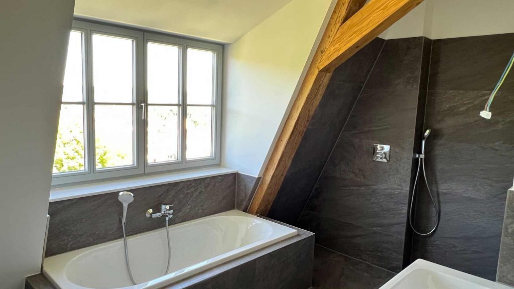 Modernes Badezimmer mit Dachschräge und Dusche Badezimmer unterm Dach mit Holzbalken, Badewanne am Fenster, Walk-in-Dusche mit schwarzen Fliesen, helle Wände
