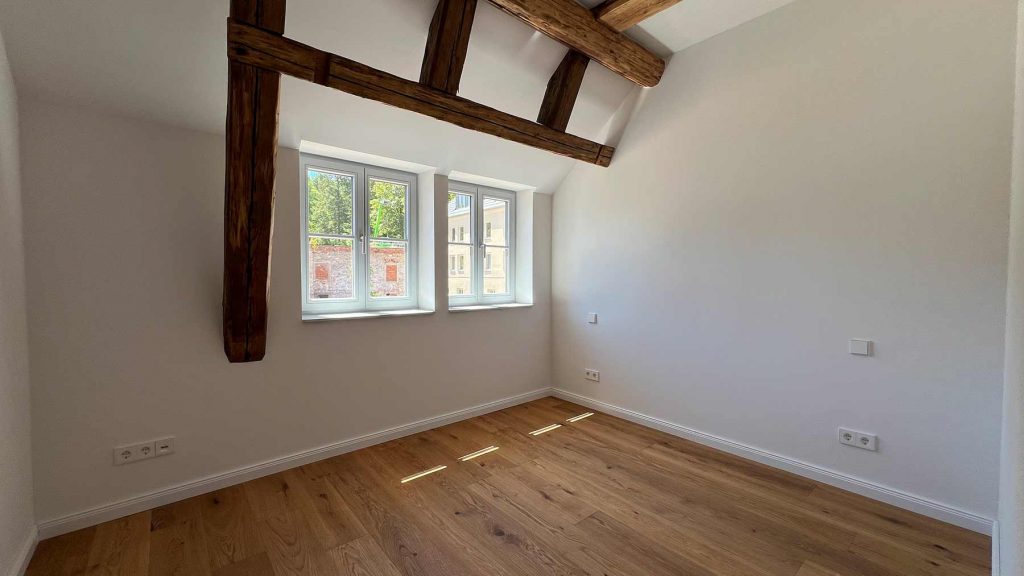 Modernes Dachzimmer Holzbalken Fenster Parkettboden Leeres Dachzimmer mit dunklen Holzbalken, hellen Wänden, Parkett und vier Fenstern zur Straße