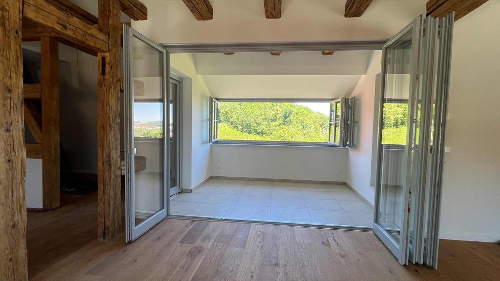 Modernes Wohnzimmer mit Terrassentüren Grün Moderner Wohnraum mit Holzbalkendecke, Glasschiebetüren zur Terrasse, Blick auf grüne Vegetation