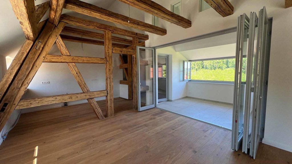 Modernes Loft mit Holzbalken und Terrassenzugang Geräumiges Wohnzimmer mit Holzdeckenbalken, Parkettboden, offener Raumaufteilung und großflächigen Glasschiebetüren zur grünen Außenterrasse