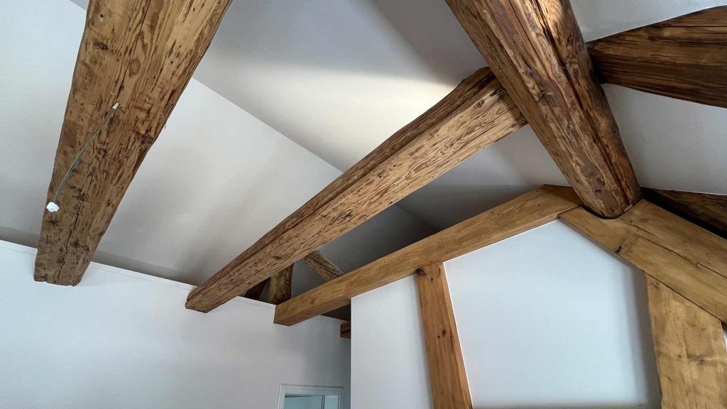 Rustikale Holzbalken Decke Wohnraum Obergeschoss Wohnraum mit massiven Holzbalken an Decke und Wand, weiße Wandflächen, Fenster im Hintergrund