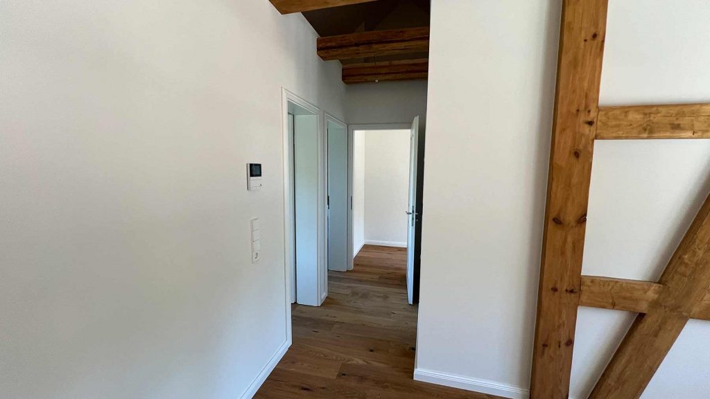 Flur Holzbalken Weiße Türen Obergeschoss Heller Flurbereich mit Holzdeckenbalken, weißen Wänden, offenen Türrahmen und Holzfußboden im Obergeschoss