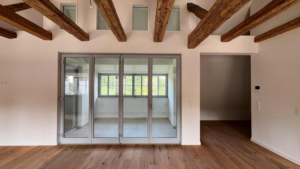 Modernes Wohnzimmer Holzbalken Glasschiebetüren Helles Wohnzimmer mit rustikalen Deckenbalken, vier Glasschiebetüren zur Terrasse und Parkettboden