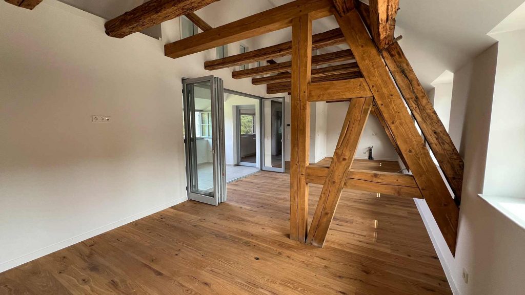 Modernes Wohnzimmer Holzbalken Dachgeschoss Offenes Wohnzimmer mit Altholzbalken, Parkettboden, Glasschiebetüren zu Terrasse und angrenzenden Räumen