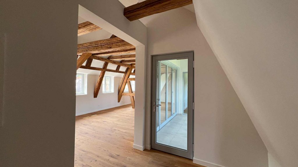 Dachgeschoss Loft Holzbalken Glastür Terrasse Geräumiges Dachgeschoss mit massiven Holzbalken, helles Parkett, weiße Wände, Glasschiebetür zur Terrasse, mehrere Fenster mit Tageslicht