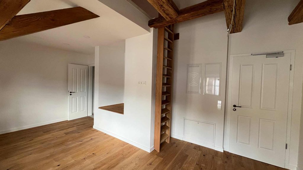 Dachgeschoss Wohnraum Holzbalken Weiße Türen Dachzimmer mit Holzdeckenbalken, Parkettboden, weißen Türen und eingebauten Regalen zwischen Balken