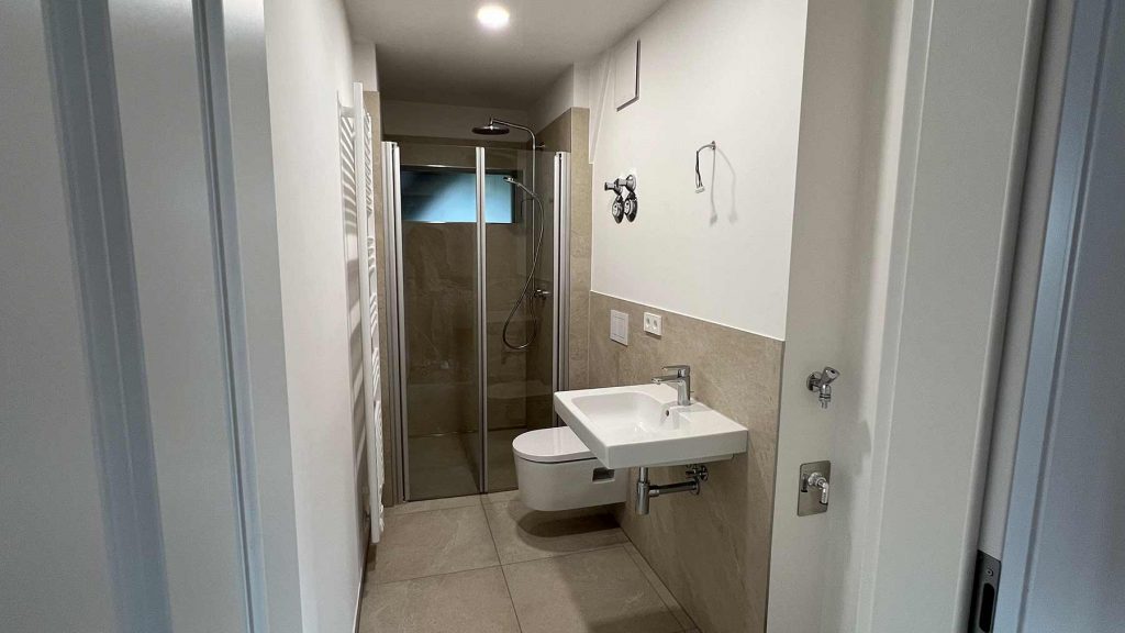 Modernes Badezimmer mit Dusche und Waschbecken Modernes Bad mit begehbarer Duschkabine, Toilette, Waschtisch und Handtuchheizer, helle Wandfliesen und dunkler Boden