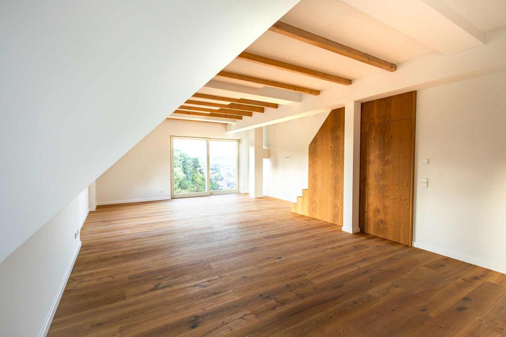7I4A4983-2 Dachgeschosszimmer mit Holzbalkendecke, Parkettboden, Glasfenstern mit Waldblick und zwei Holztüren