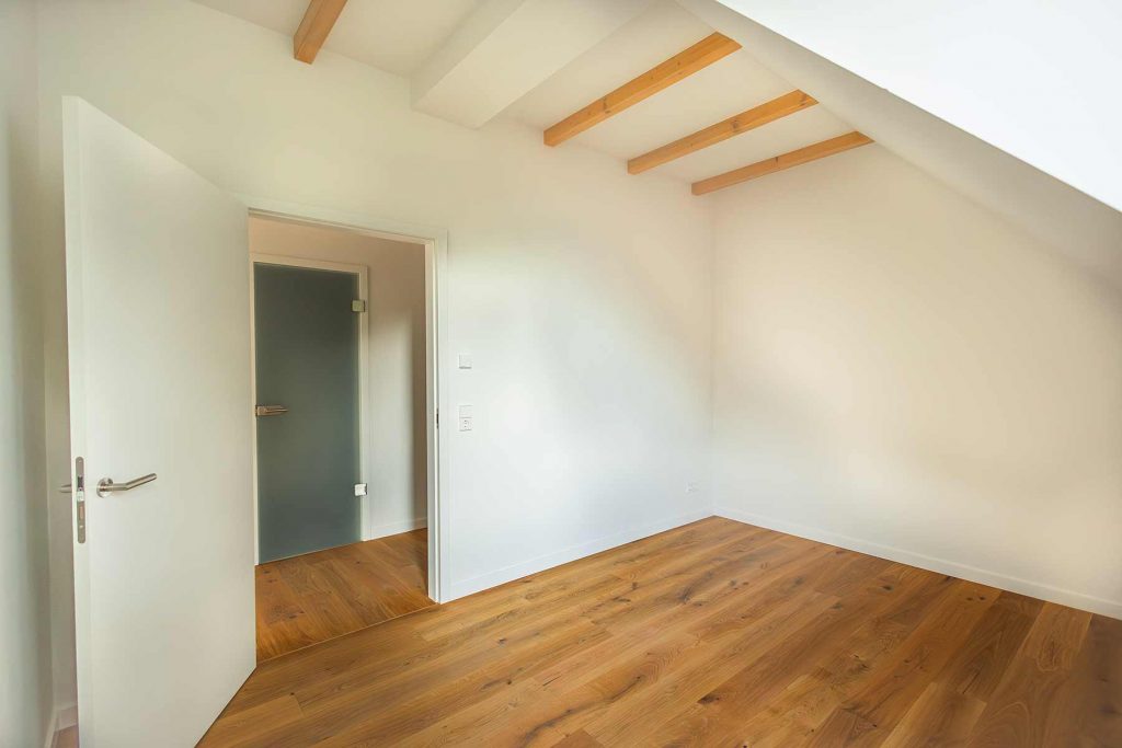 7I4A5067-2 Dachgeschossraum mit Holzbalken, Holzboden, weißen Wänden und zwei Türen zur Küche und Bad