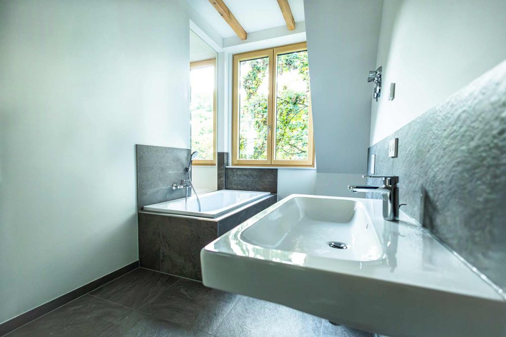 7I4A5097 Modernes Badezimmer mit Dachfenstern, weißem Waschbecken rechts, dunkler Badewanne links und grauer Natursteinverkleidung