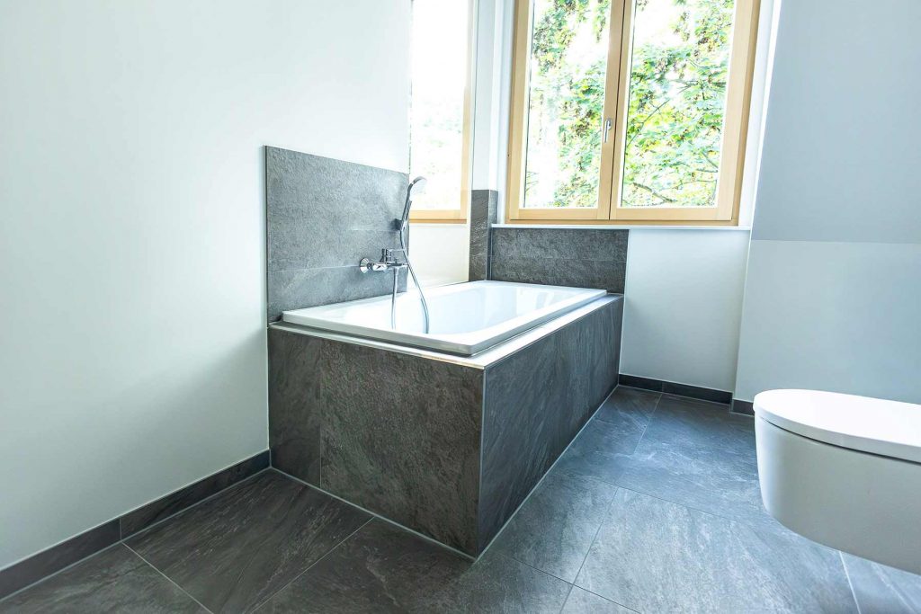 7I4A5104 Modernes Badezimmer mit grauem Naturstein-Whirlpool, Regendusche, Toilette und Fensterblick ins Grüne