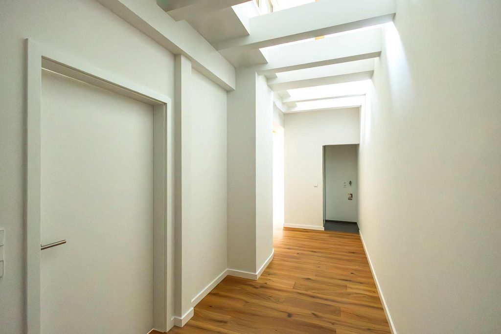 7I4A5143 Flur mit Holzboden, weißen Wänden, Dachfenstern und mehreren Türen im Dachgeschoss einer Wohnung