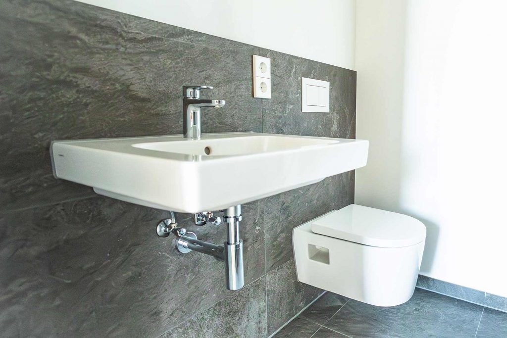 7I4A5154 Modernes Badezimmer mit weißem Waschbecken, Wandtoilette und grauer Natursteinfliesen-Rückwand