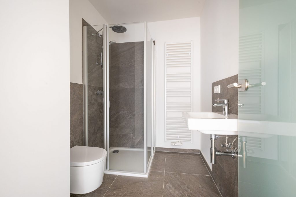 Modernes Badezimmer Grau Weiß Dusche Modernes Badezimmer mit Toilette links, begehbarer Duschkabine mit Glastüren in der Mitte, Waschbecken rechts und Handtuchheizer an der Wand