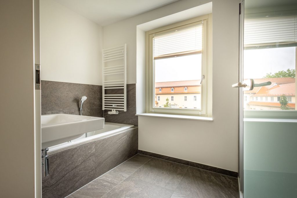 Modernes Badezimmer Graue Fliesen Stadtblick Geräumiges Badezimmer mit dunkelgrauer Steinoptik-Verkleidung, freistehende Wanne, Handtuchheizer, Fenster mit Stadtblick, Glastür zur Dusche rechts