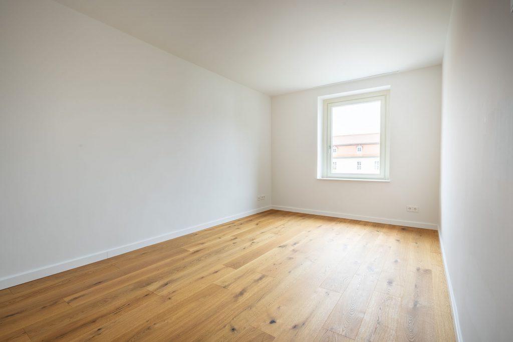 Leeres Zimmer Holzboden Fenster Wohnhaus Helles Zimmer mit Parkettboden, weiße Wände, Fenster mit Blick auf Wohngebäude, Steckdosen an der Wand sichtbar