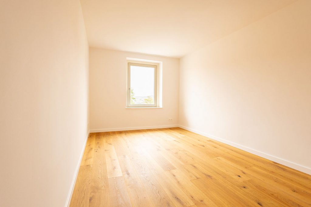 Leeres Zimmer Eichenparkett Fenster Ausblick Helles Wohnzimmer mit Holzboden, cremefarbenen Wänden und Fenster mit Ausblick auf Landschaft