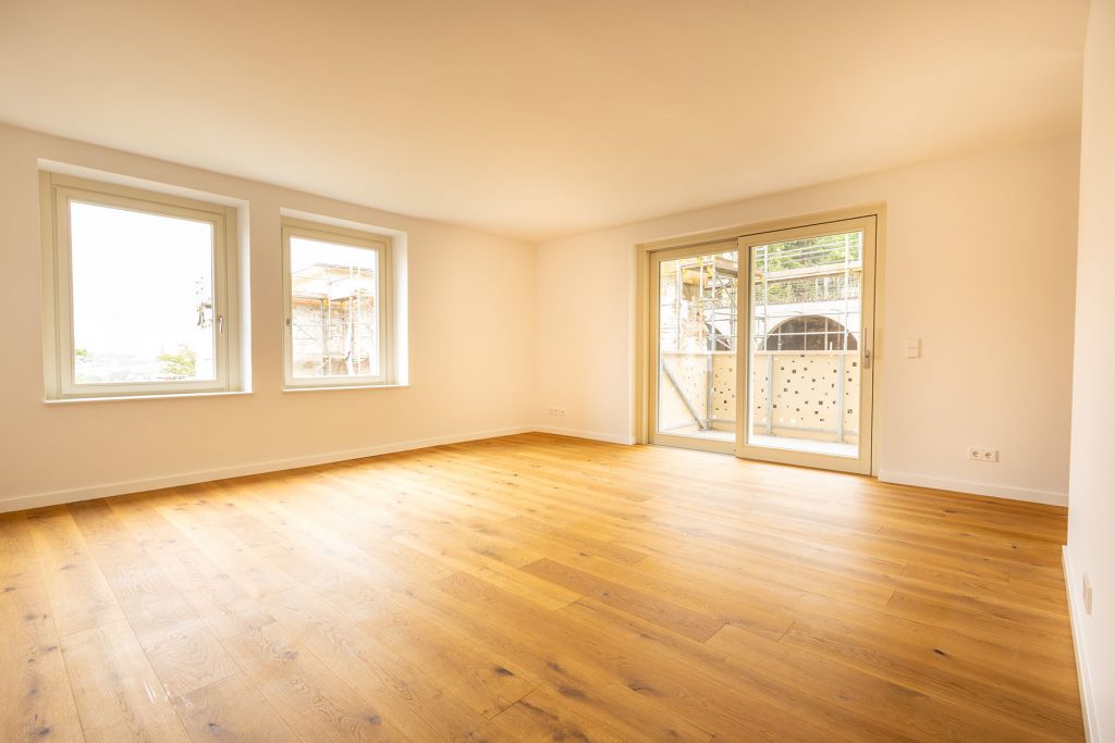 Helles Wohnzimmer Eichenparkett Balkontür Ausblick Leeres Wohnzimmer mit Holzboden, zwei Fenster links, Glasschiebetür rechts zu Balkon, beige Wände, helle Decke
