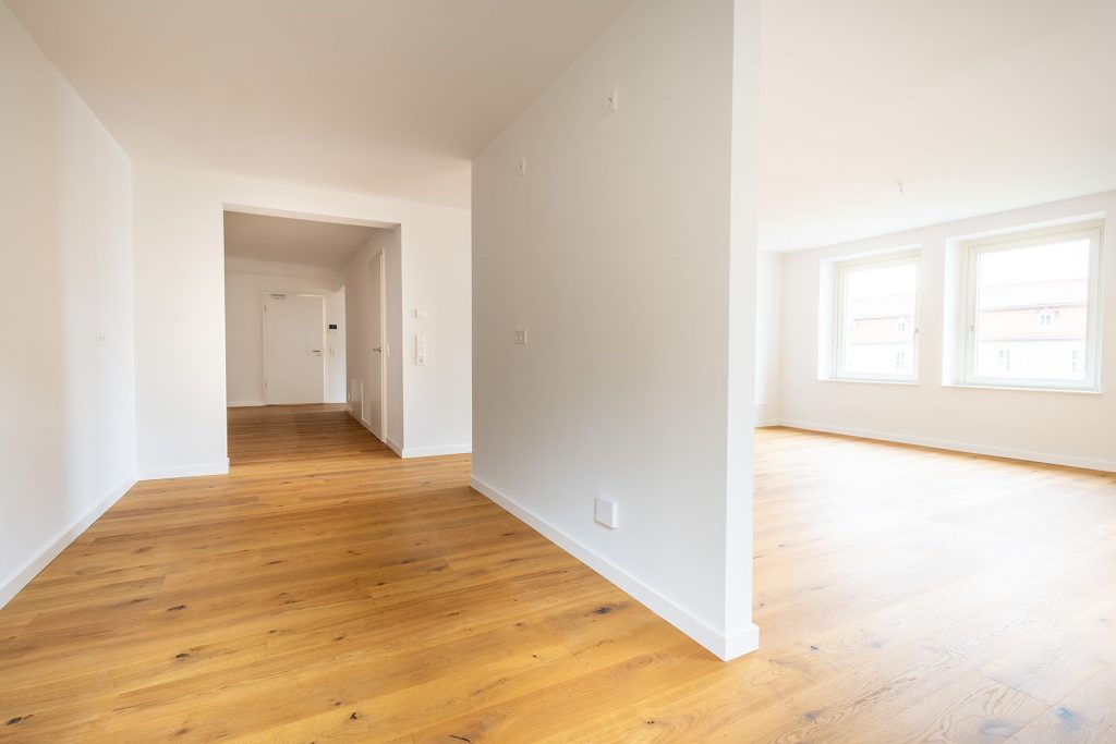 Leeres Wohnzimmer Holzboden Helle Wohnung Heller Wohnbereich mit Eichenparkett, weißen Wänden, zwei Fenstern und offener Raumaufteilung in Obergeschoss-Wohnung