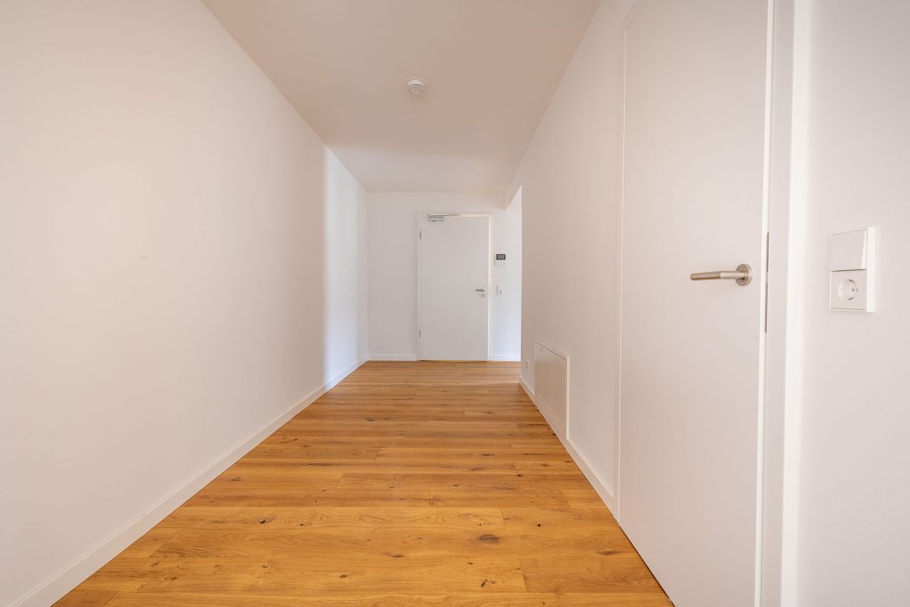 Moderner Flur mit Parkett-Boden Wohnung Heller Korridor mit Holzdielen, weiße Wände, Tür rechts, Aufzug am Ende, Lichtschalter und Steckdose an der Wand
