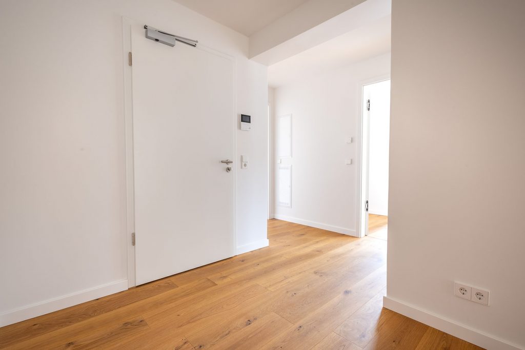 Moderner Flur Holzboden weiße Türen Wohnung Heller Flurbereich mit Eichenparkett, weiße Innentüren, Thermostat an der Wand, offene Raumverbindung zum Wohnbereich