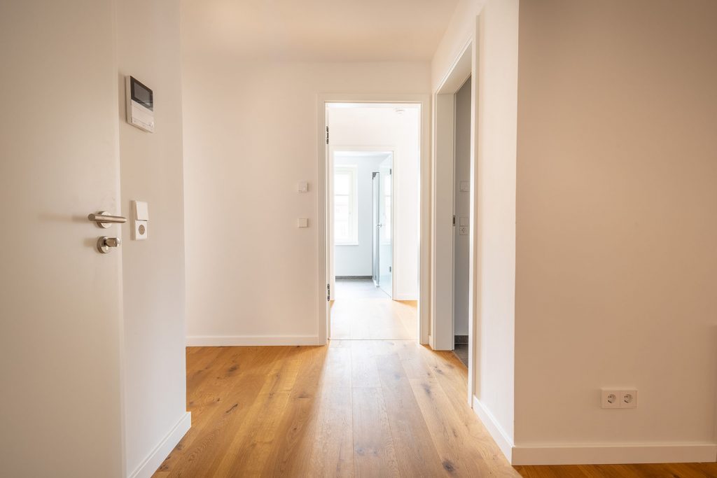 Moderner Flur mit Parkett und weißen Türen Heller Korridor mit Holzboden, mehreren weißen Türen links und rechts, Durchgang zu Wohnbereich, Schalter und Steckdosen an den Wänden
