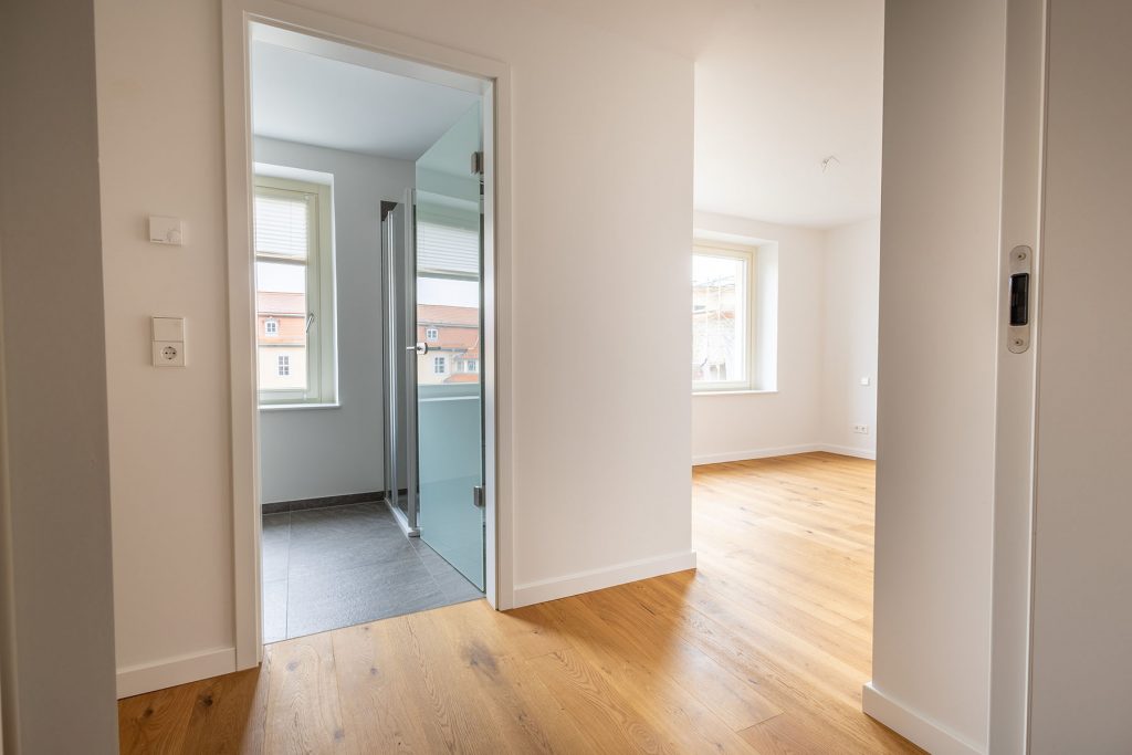 Moderne Wohnung Holzboden Stadtblick Neubau Moderner Flur mit Eichenparkett, glasgeteiltes Badezimmer links, helles Wohnzimmer rechts, großzügige offene Raumaufteilung mit Fensterblick auf Stadt